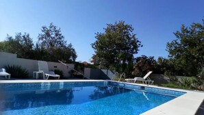 A rectangular swimming pool with clear blue water, surrounded by a white deck. There are lounge chairs and a small staircase leading to a covered area. - Apartments Villa Dona (Vela Luka)