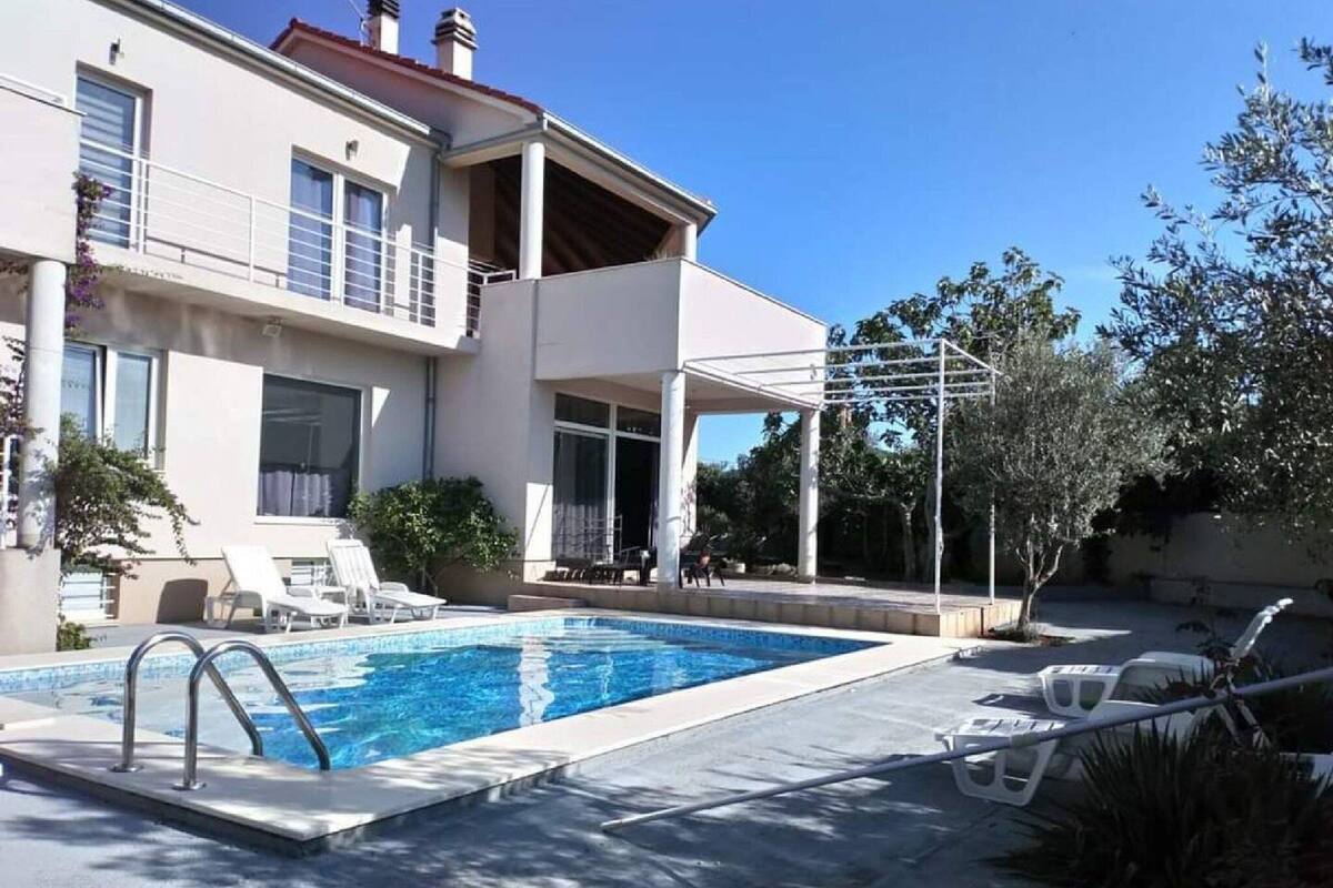 Una casa moderna de dos pisos con piscina, mobiliario exterior y una pérgola.