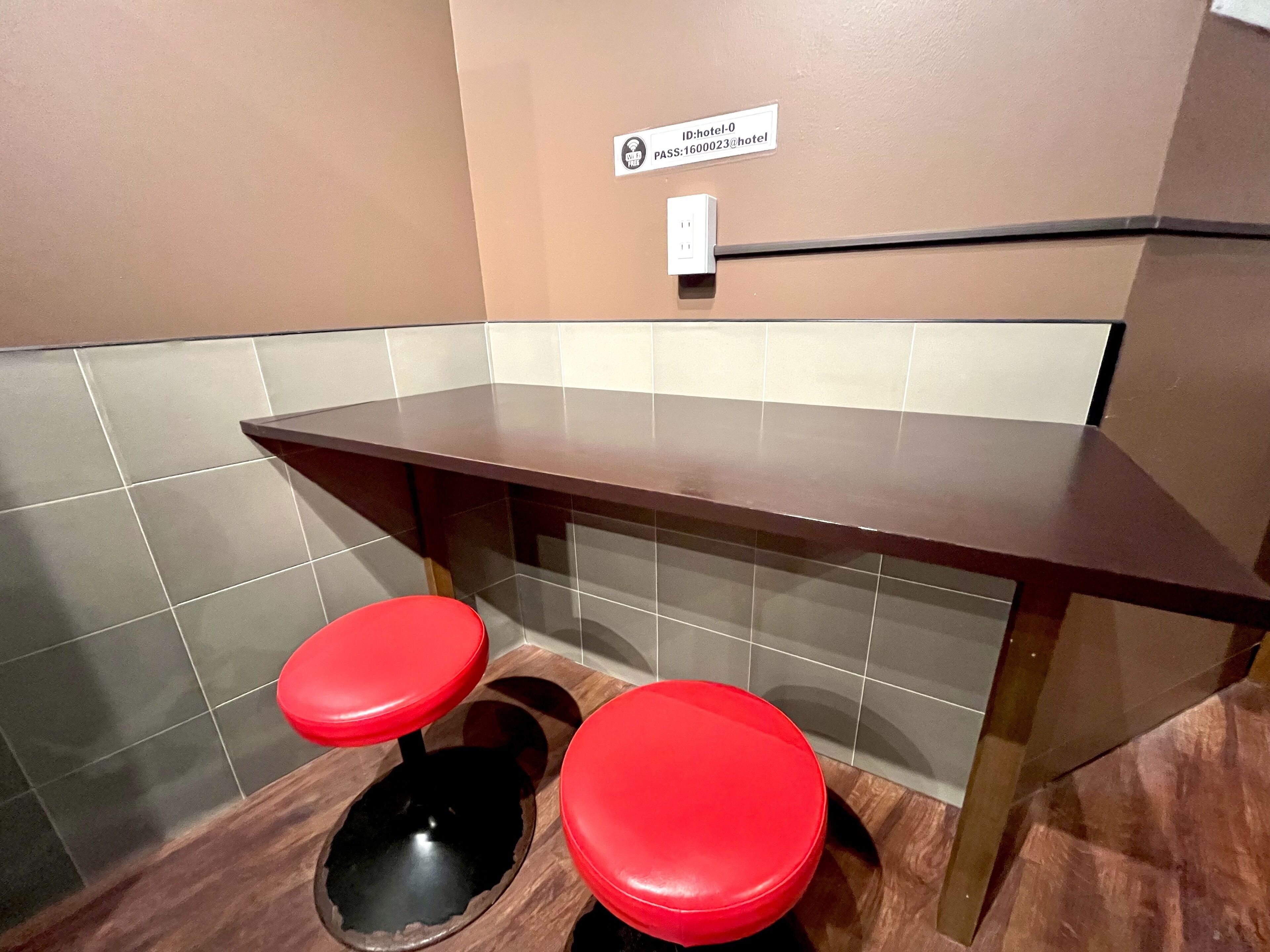 A restroom with two red stools, a brown counter, and a sign above the counter.