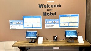 A reception desk with a 'Welcome to our Hotel' sign, two computer monitors displaying booking websites, and a 'Check-in Guide' poster. - Shinjuku Nikka Hotel - Hostel  (Tokyo)