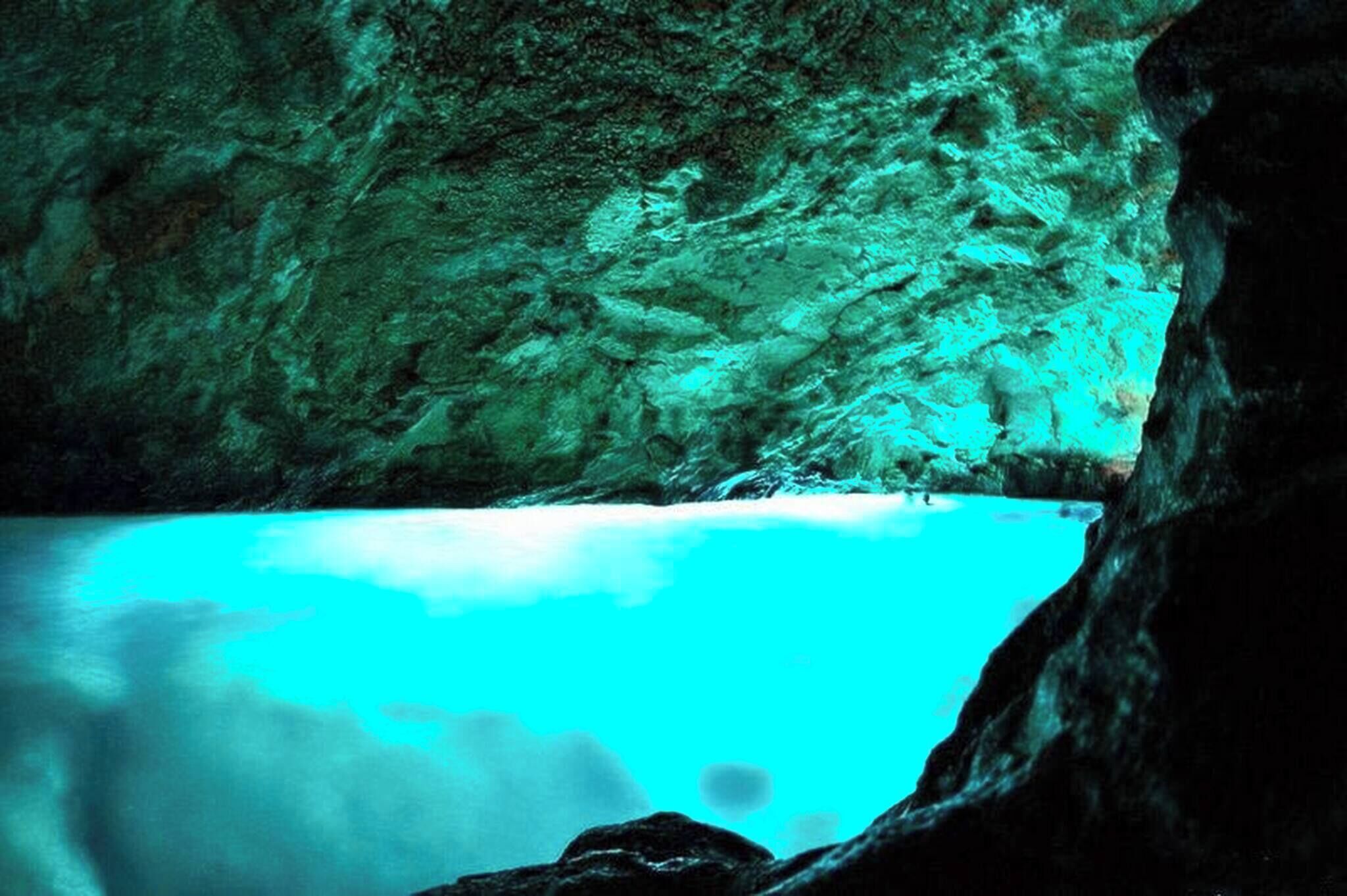 A cave with turquoise water and rocky walls.