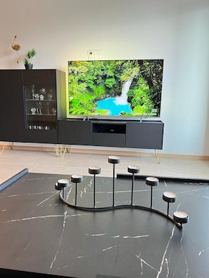 A modern living room with a flat-screen TV, a dark entertainment unit, and a marble coffee table with bar stools. - Apartments Jelena (Dubrovnik)