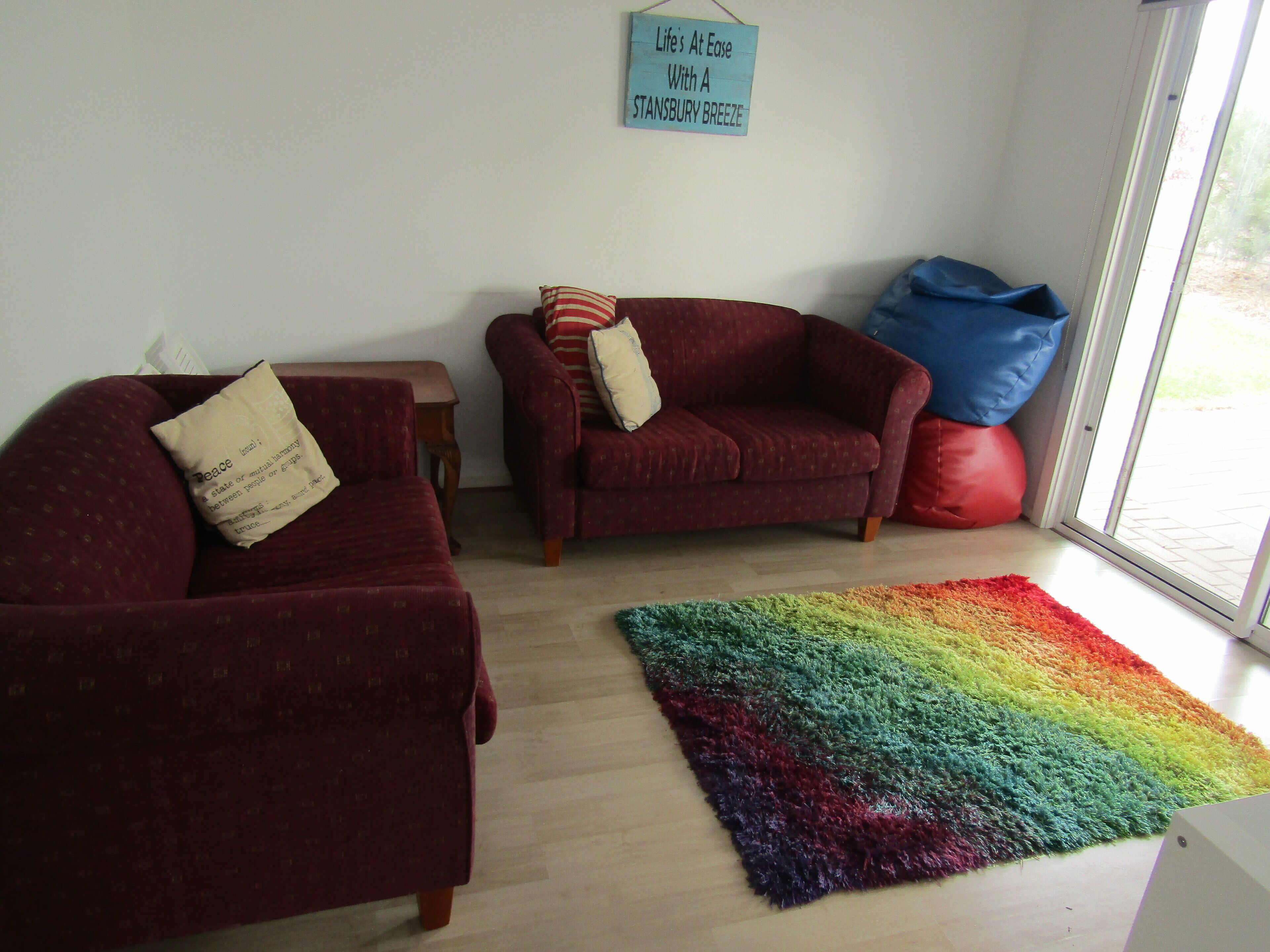 A living room with two red sofas, a small wooden table, a colorful rug, and a sign on the wall.