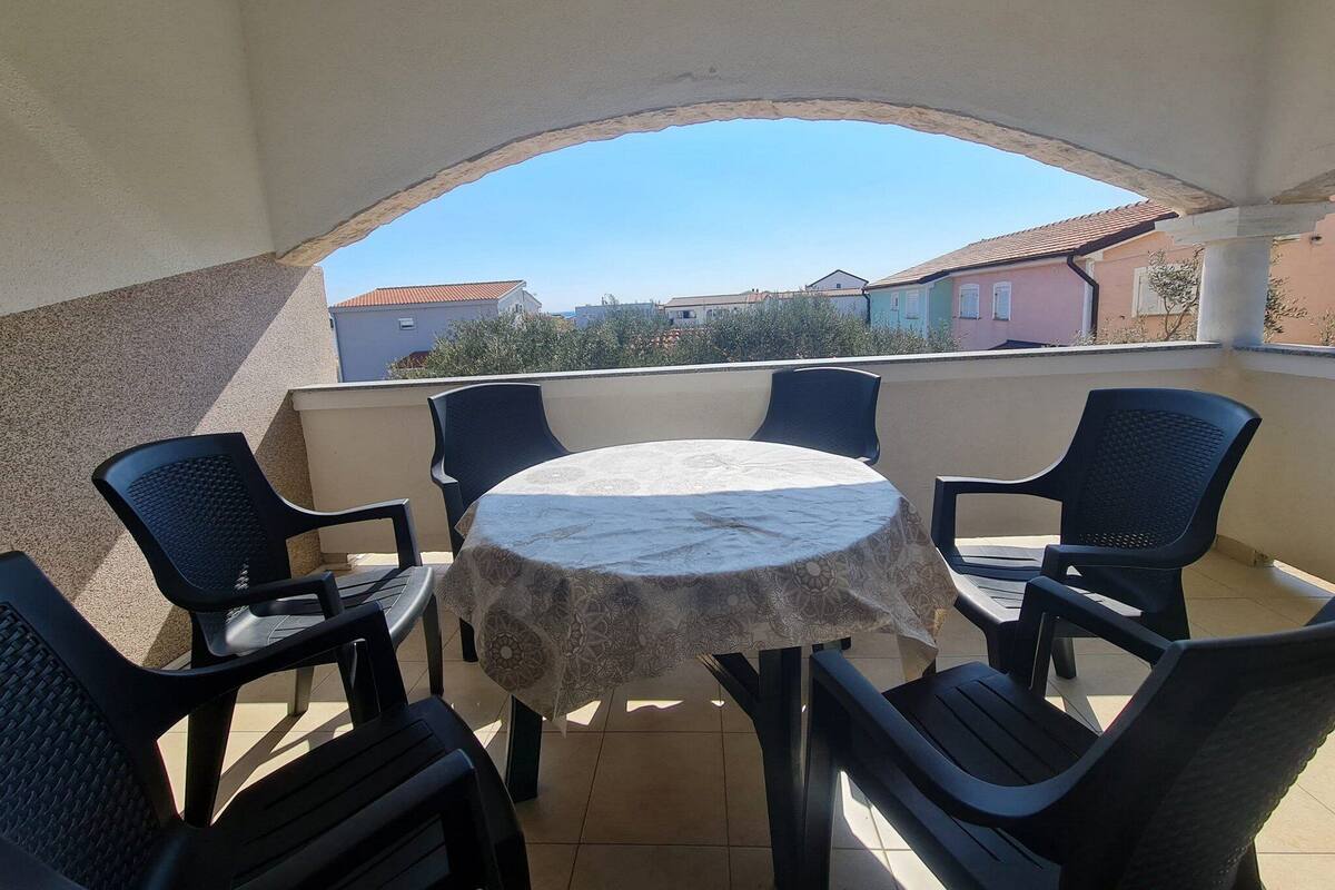 A covered outdoor seating area with a table and chairs, a view of buildings in the background, and a tiled floor.