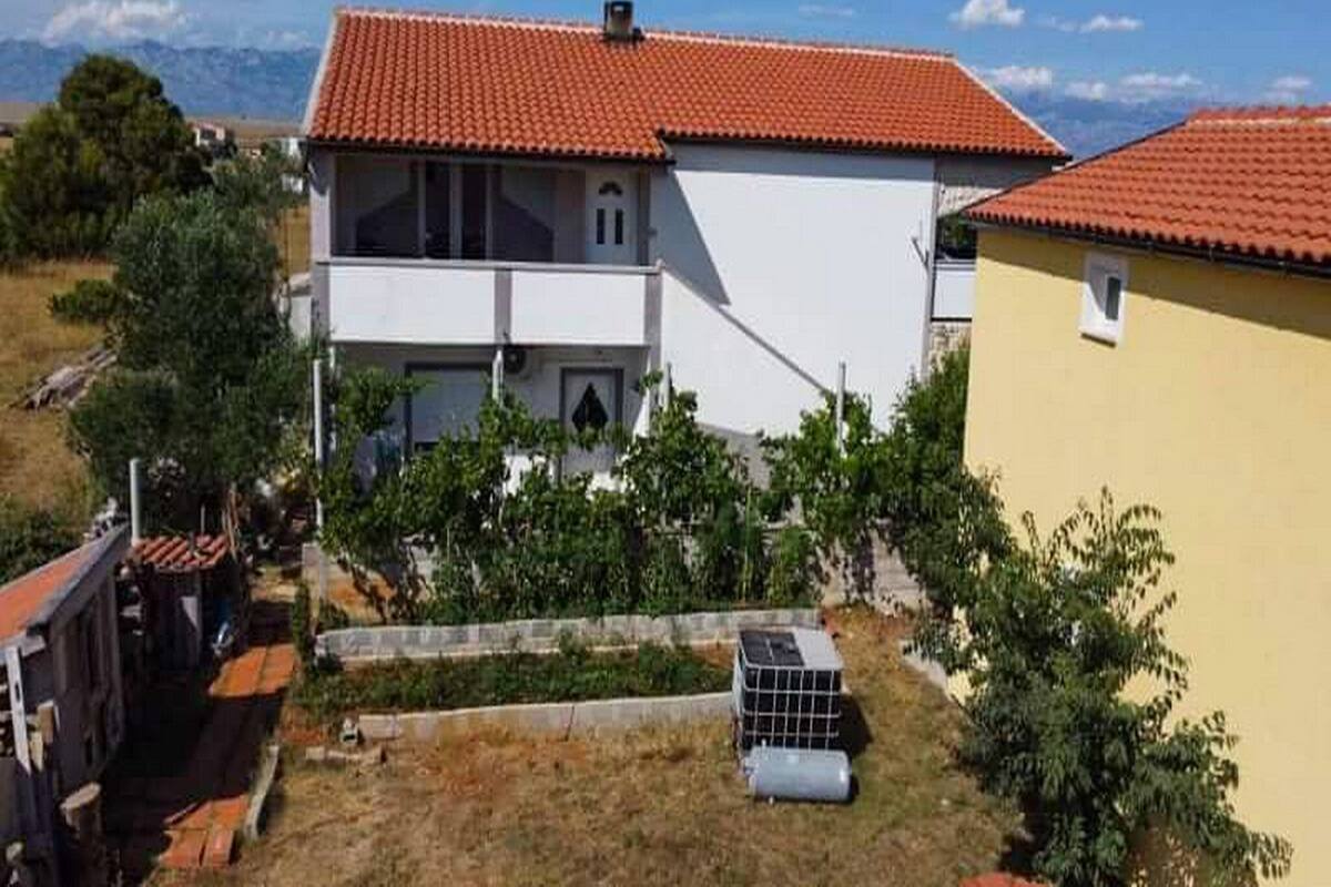 A two-story house with a red-tiled roof, a balcony, and a small garden area.