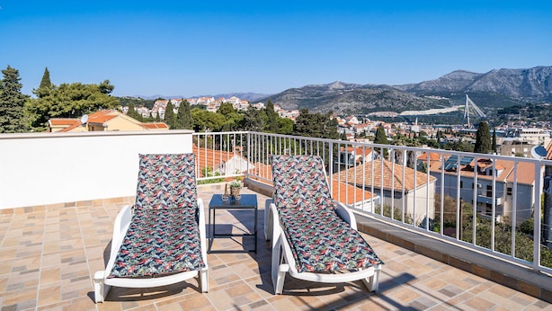A rooftop terrace with two sun loungers, a small table, and a view of a cityscape and mountains. - Apartment Dorica (Dubrovnik)