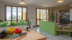 A spacious living area with a green sofa, a wooden table with a bottle and glasses, and a TV on a wooden cabinet. - Crocus 1 con piscina by Wonderful Italy (Soiano del Lago)