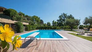 A rectangular swimming pool with a wooden deck, surrounded by greenery and a clear blue sky. - Crocus 1 con piscina by Wonderful Italy (Soiano del Lago)
