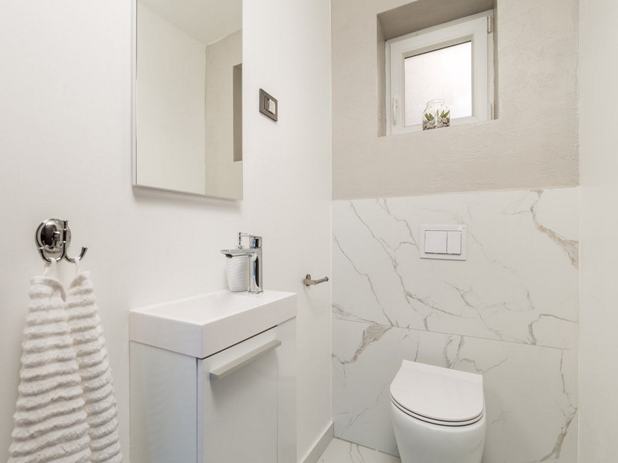 A bathroom with a white vanity, a toilet, a mirror, and a small window with a plant.