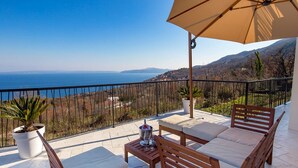 A balcony with a view of the sea, a wooden table with a glass, and two wooden chairs. - Villa Corichi (Opatija)