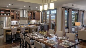A modern kitchen with a central island, dining area with set tables, and large windows with curtains.