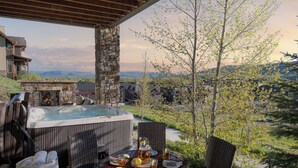 A hot tub with lounge chairs, a table with drinks, and a stone fireplace.