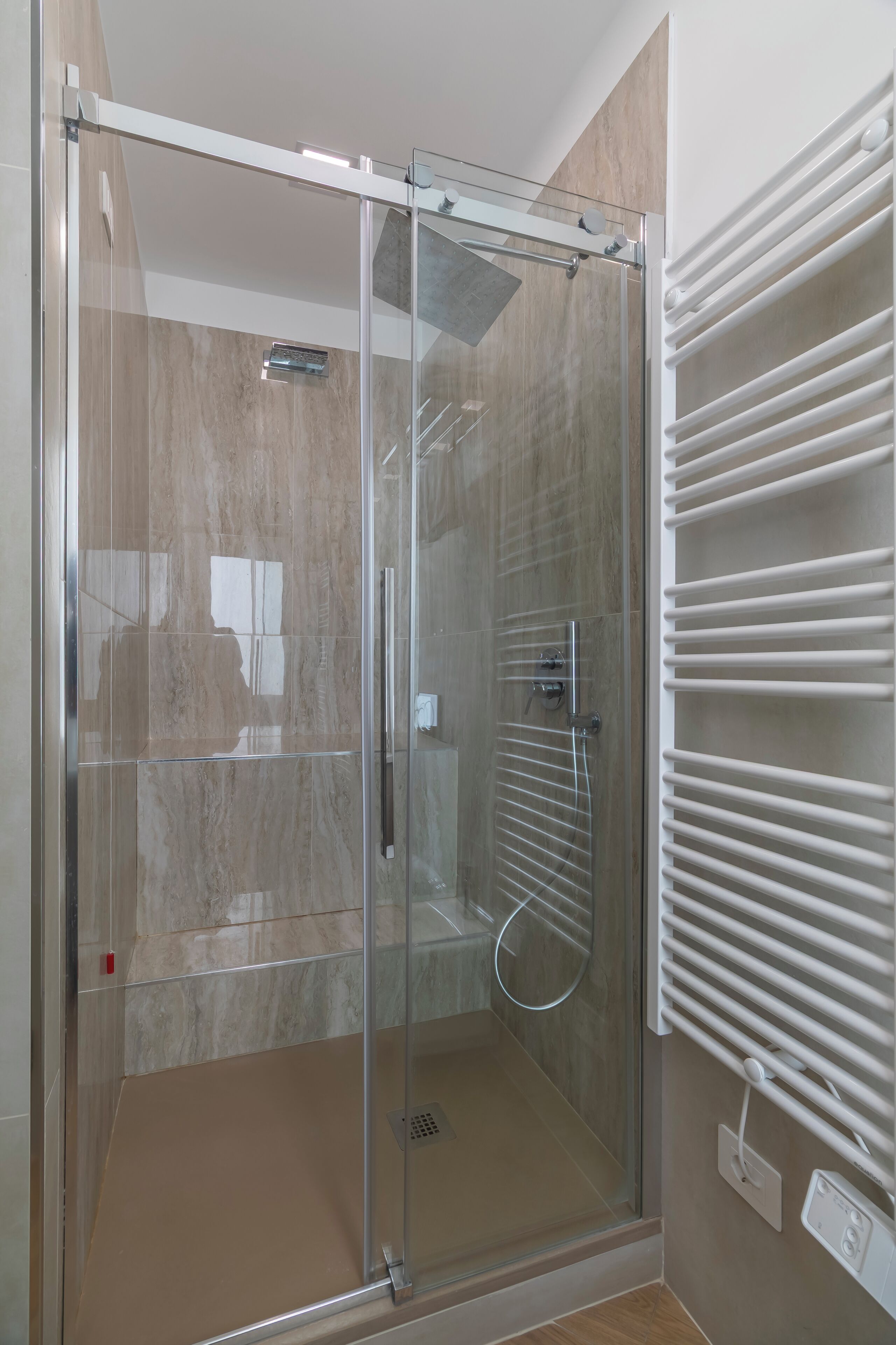 A glass-enclosed shower with a white towel rack and a control panel.