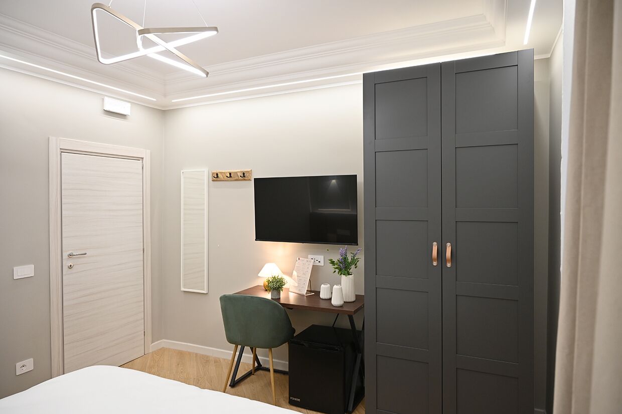 Een slaapkamer met een bed, een bureau met stoel, een televisie, een kledingkast en een plafondlamp.
