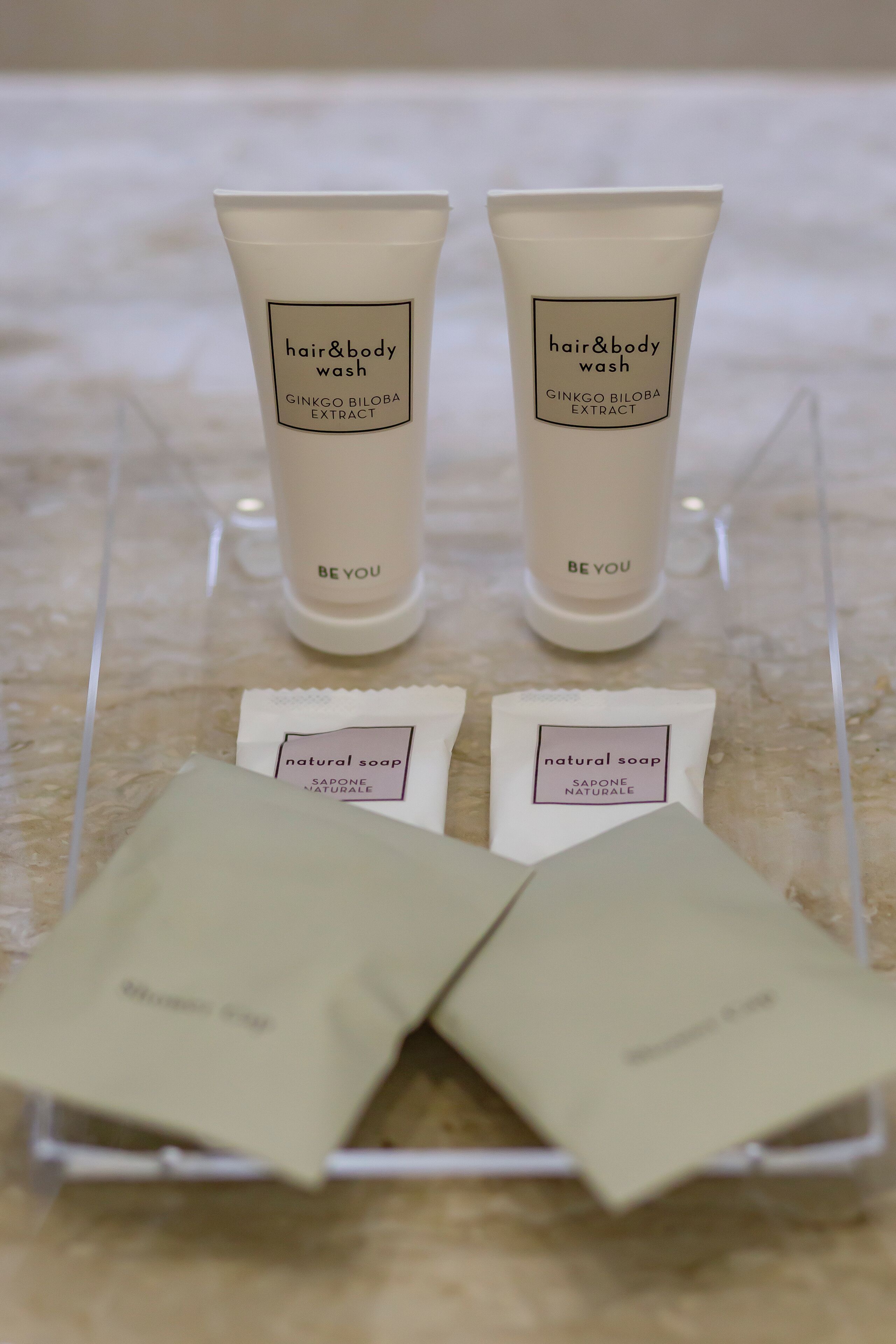 Dos tubos de jabón para cabello y cuerpo y dos paquetes de jabón natural sobre un expositor transparente.