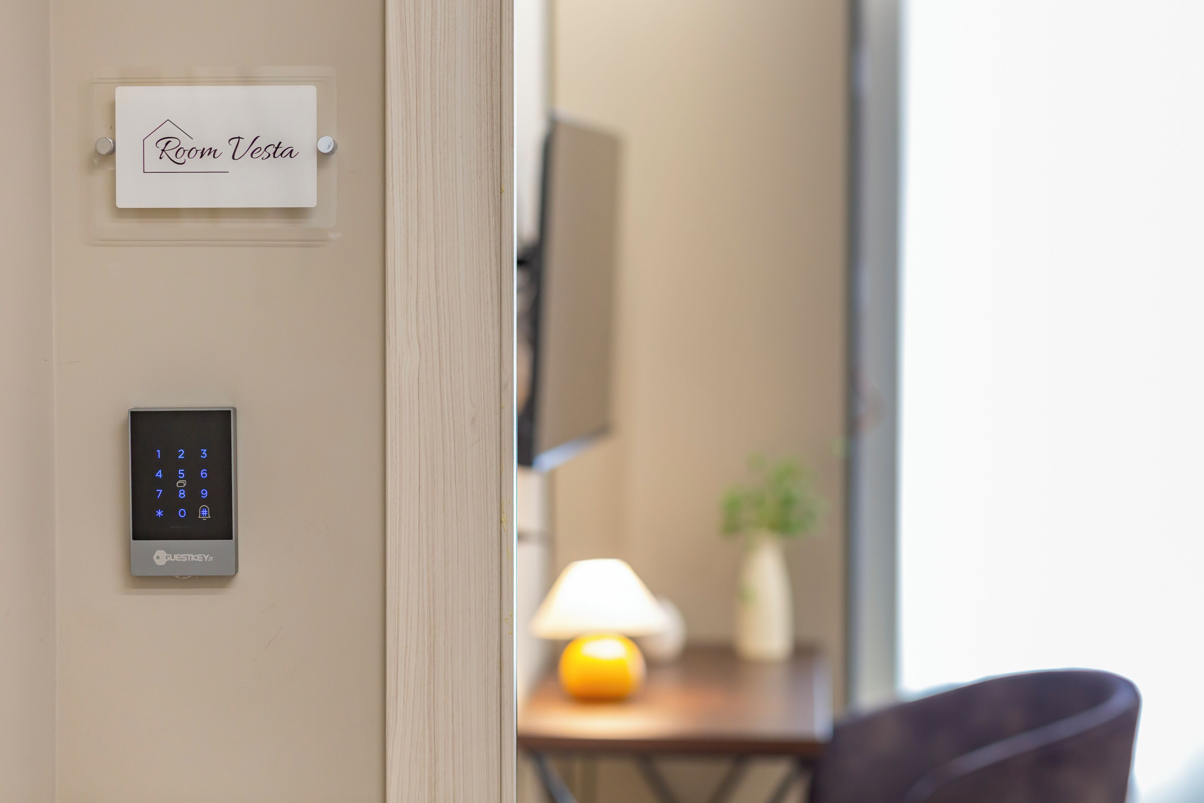 A room with a digital lock, a sign reading 'Room Vesta,' and a lamp on a table.
