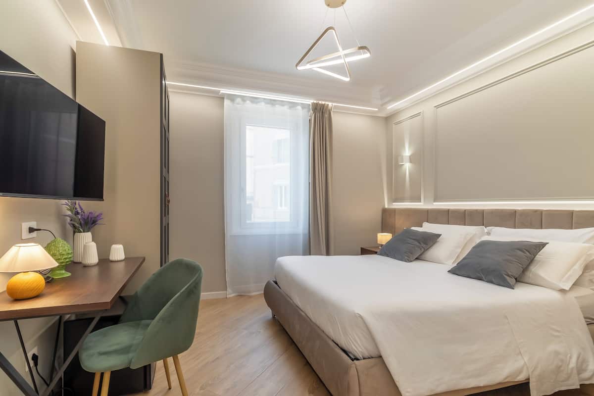 Una habitación de hotel con una cama, un escritorio con lámpara, una silla y un televisor.