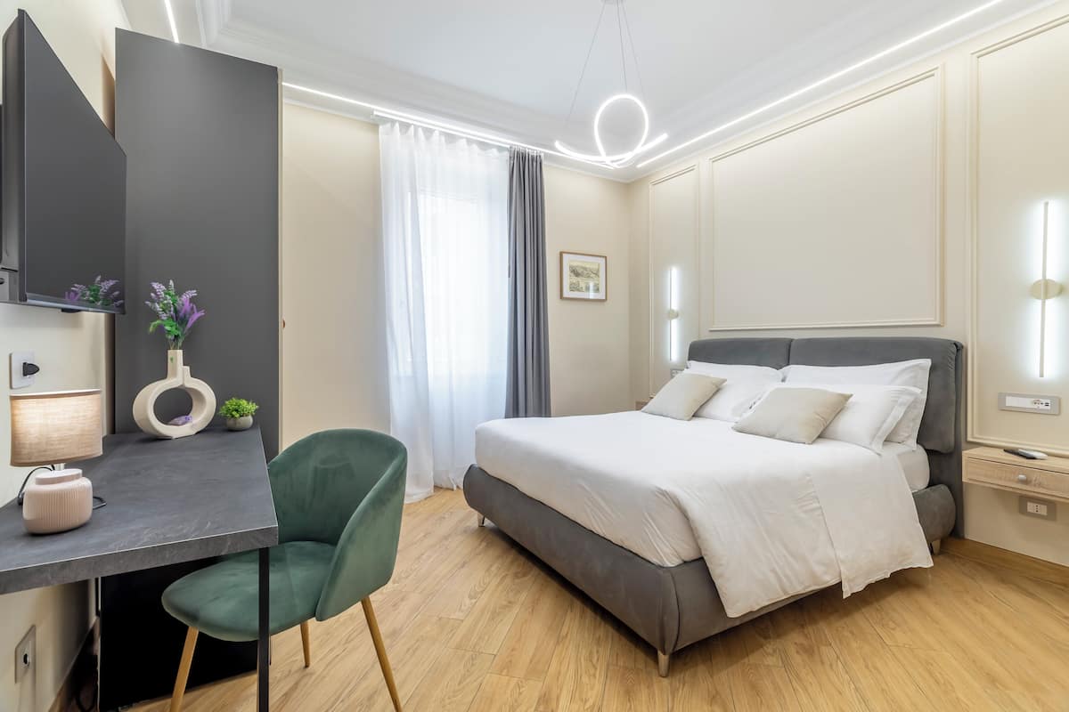 Una habitación de hotel moderna con cama, escritorio, silla y un ventanal con cortinas.
