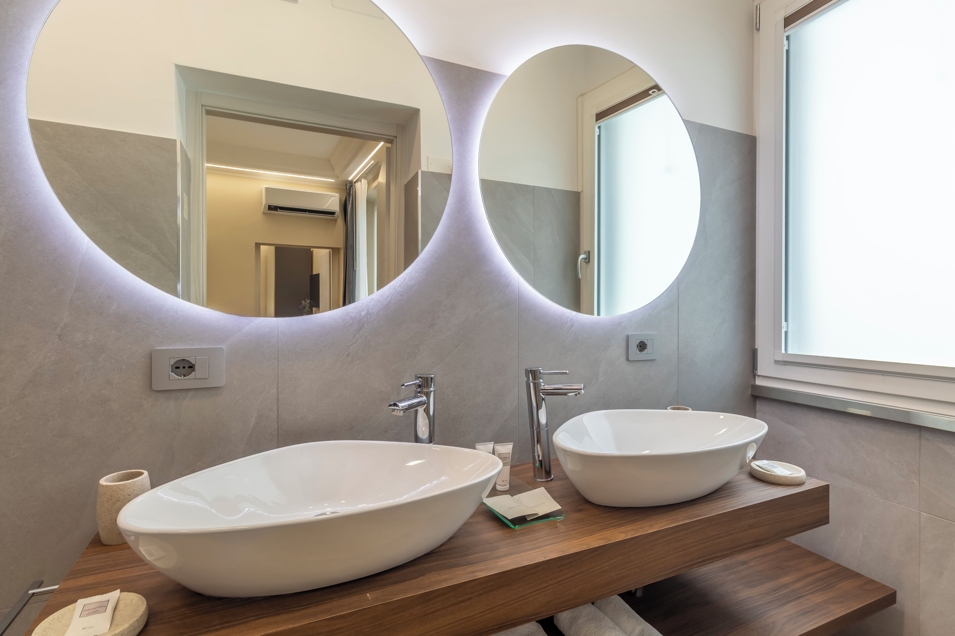 Un baño moderno con dos lavamanos tipo recipiente, un mueble de tocador de madera y un espejo grande con marcos circulares.