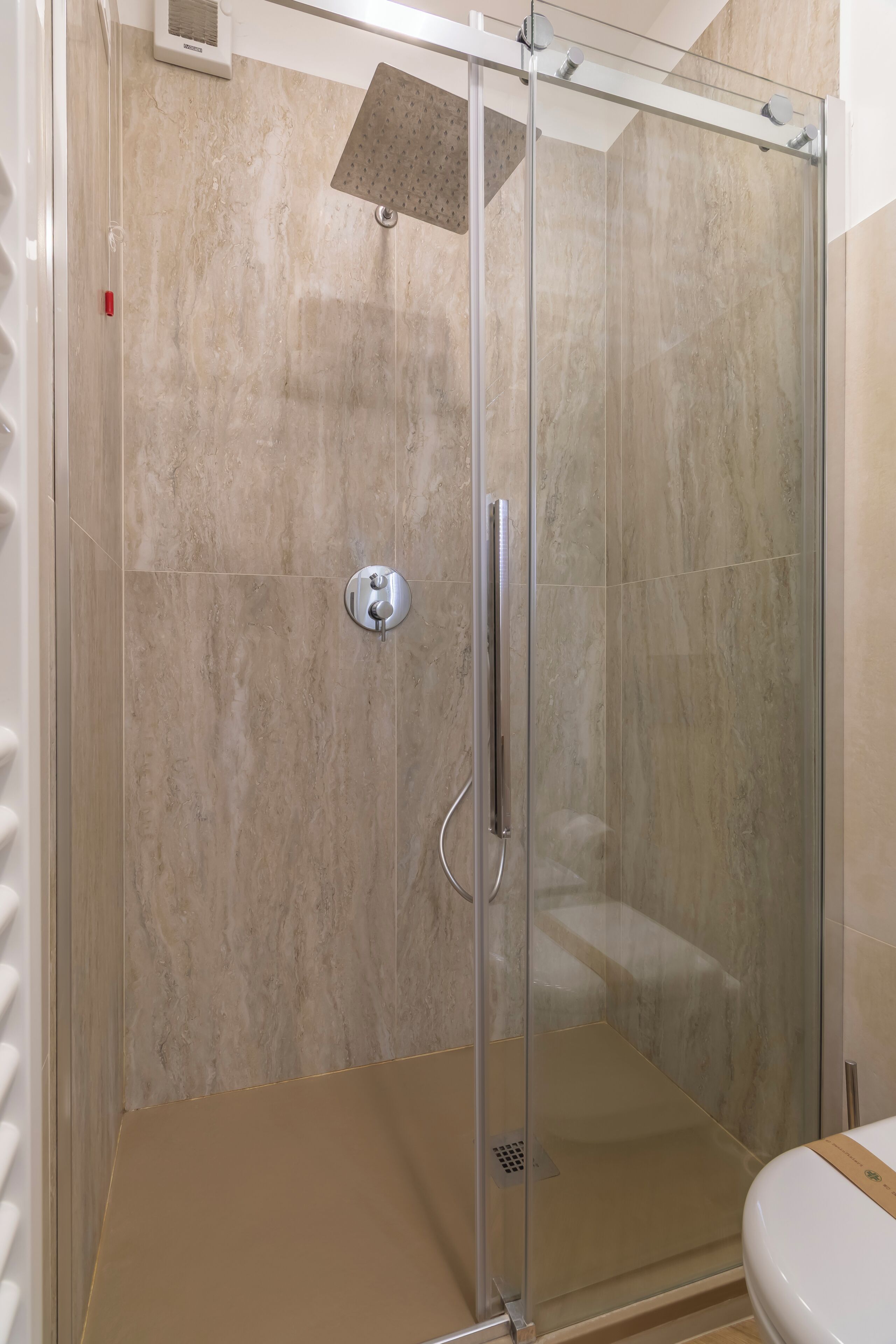 A glass-enclosed shower with a control panel, a white toilet, and beige tiled walls.
