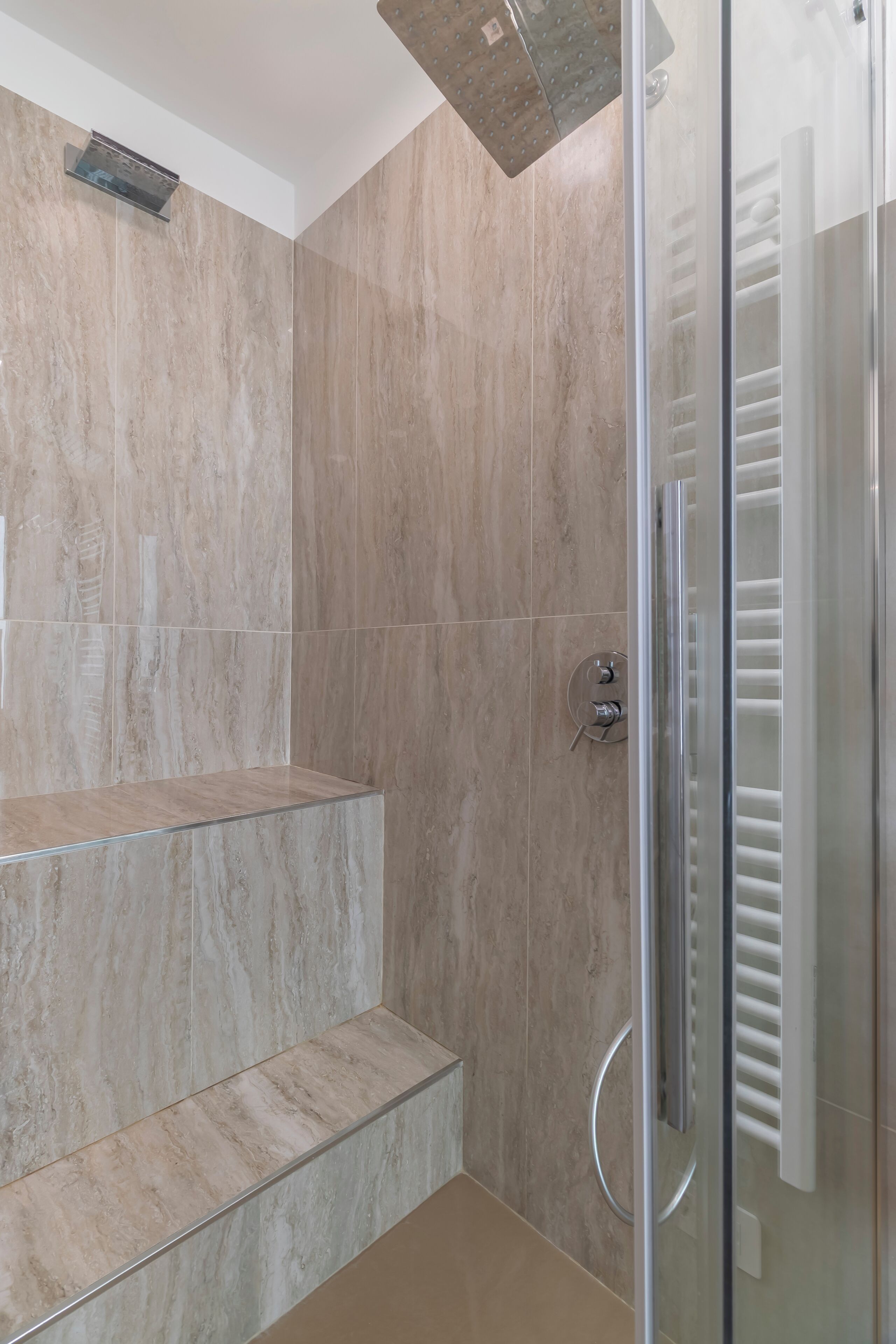 A modern bathroom with a glass shower enclosure, a built-in bench, and a towel rack.