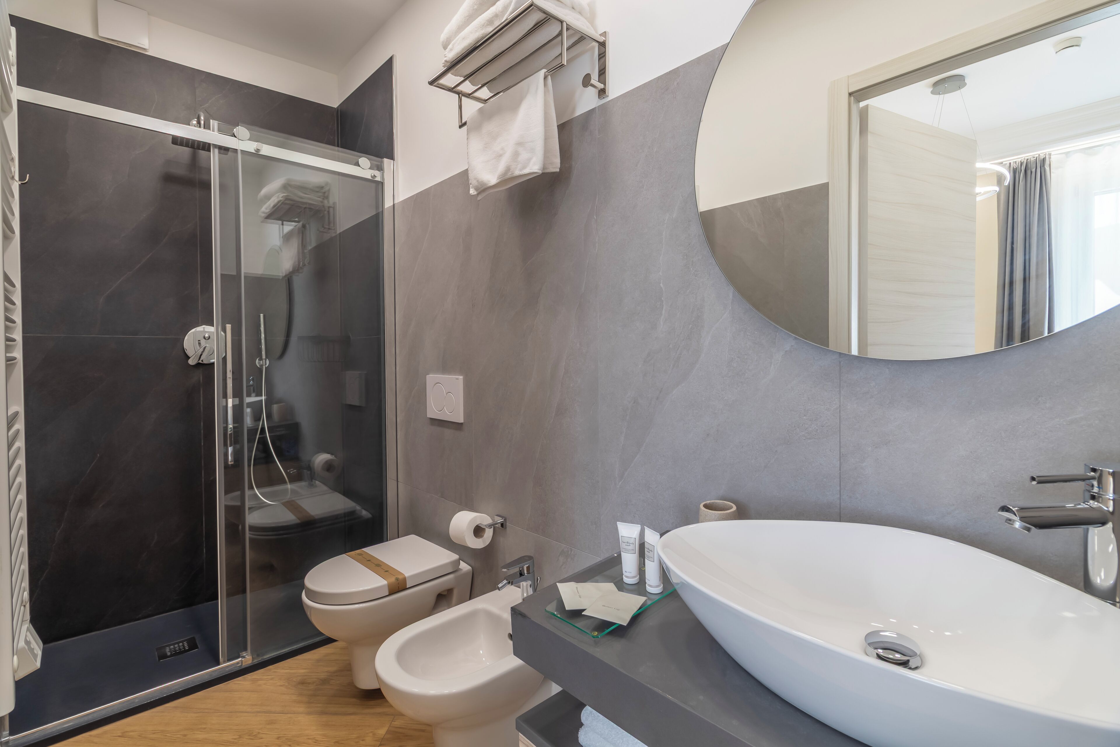 A modern bathroom with a glass-enclosed shower, a bidet, a toilet, and a large oval sink.
