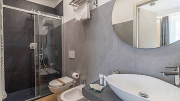 A modern bathroom with a glass-enclosed shower, a bidet, a toilet, and a large oval sink.