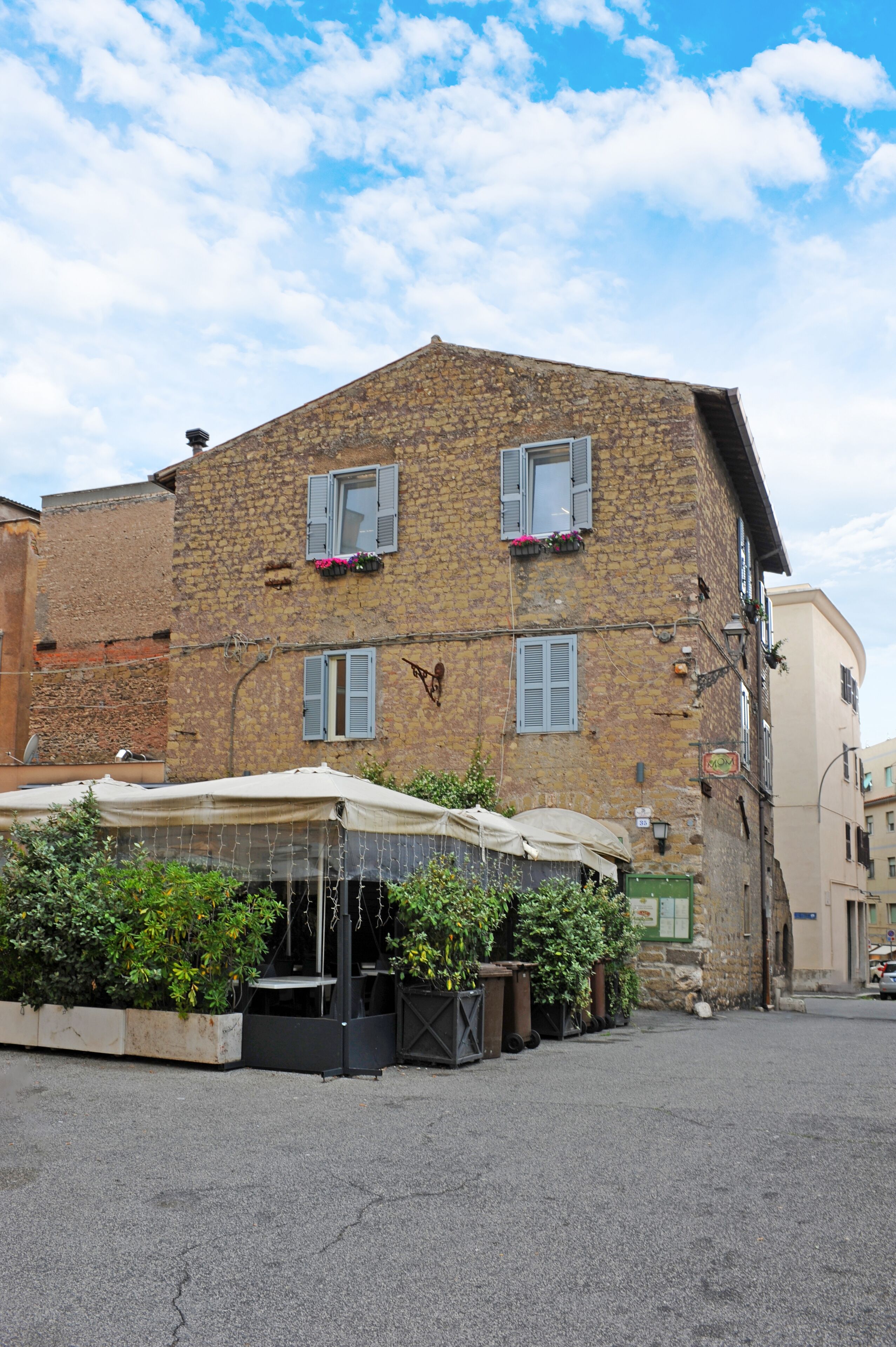 A stone building with two windows, a covered outdoor seating area, and a street in front.