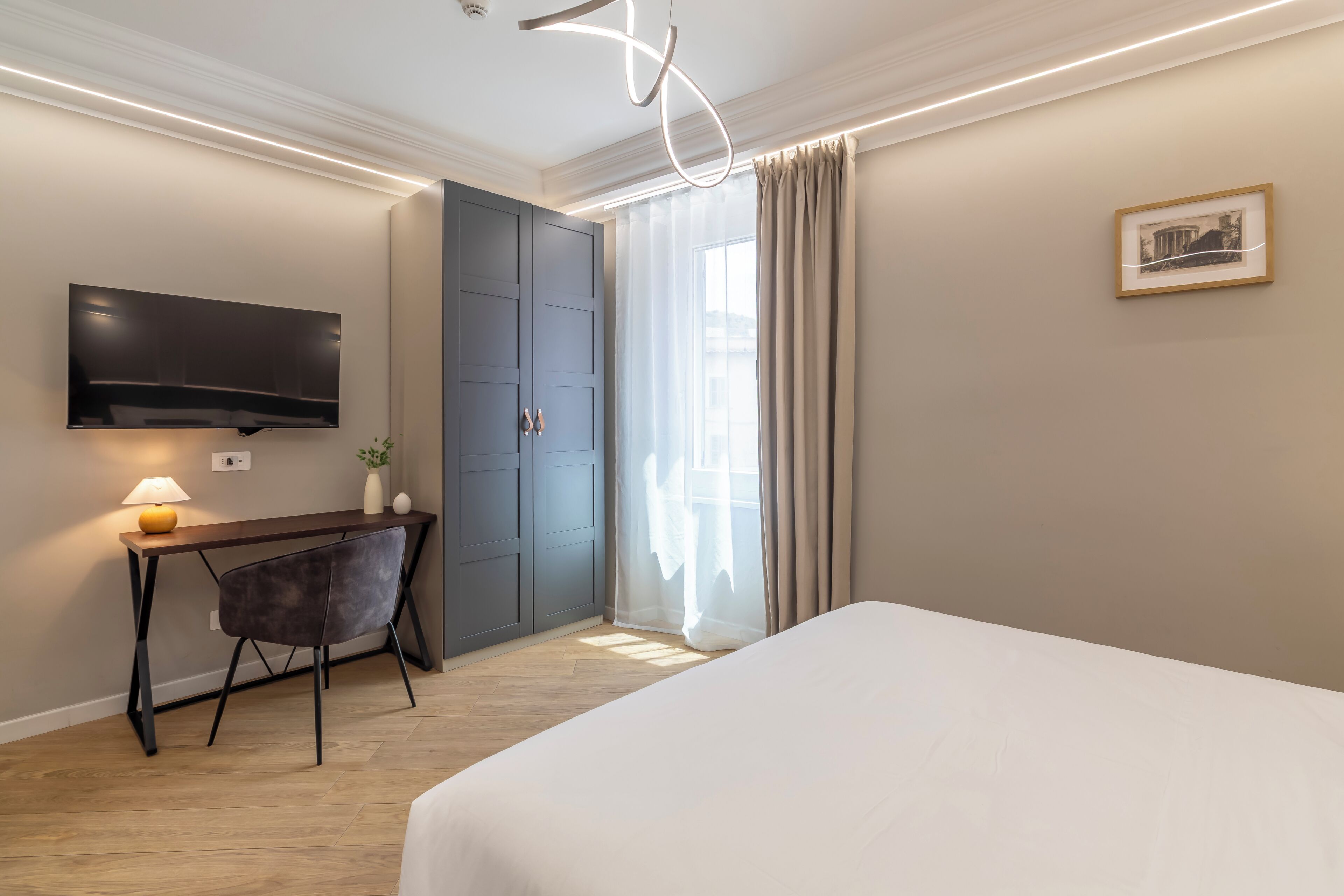Una habitación de hotel con una cama, un escritorio con silla, un televisor montado en la pared y una puerta.