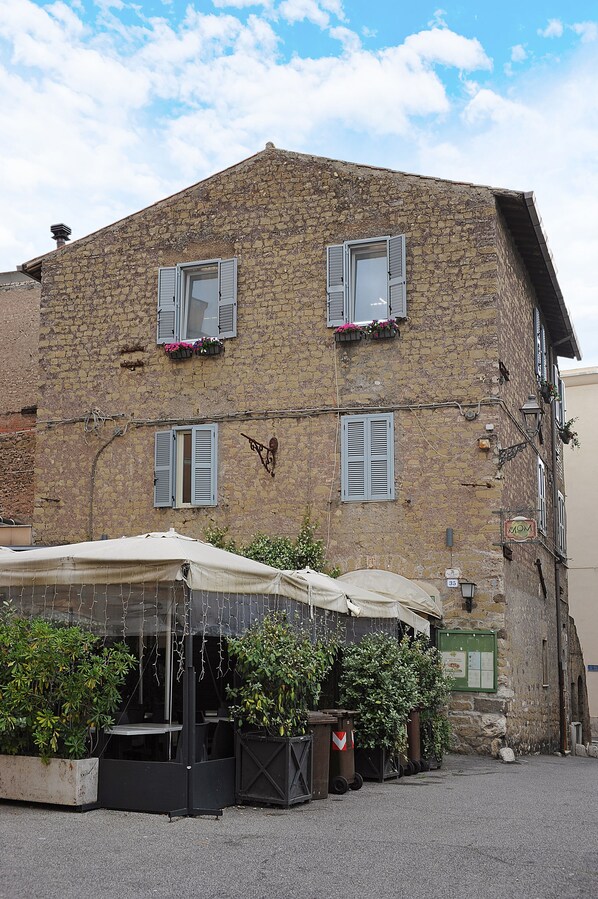 A stone building with shutters, a covered outdoor seating area, and a green signboard.