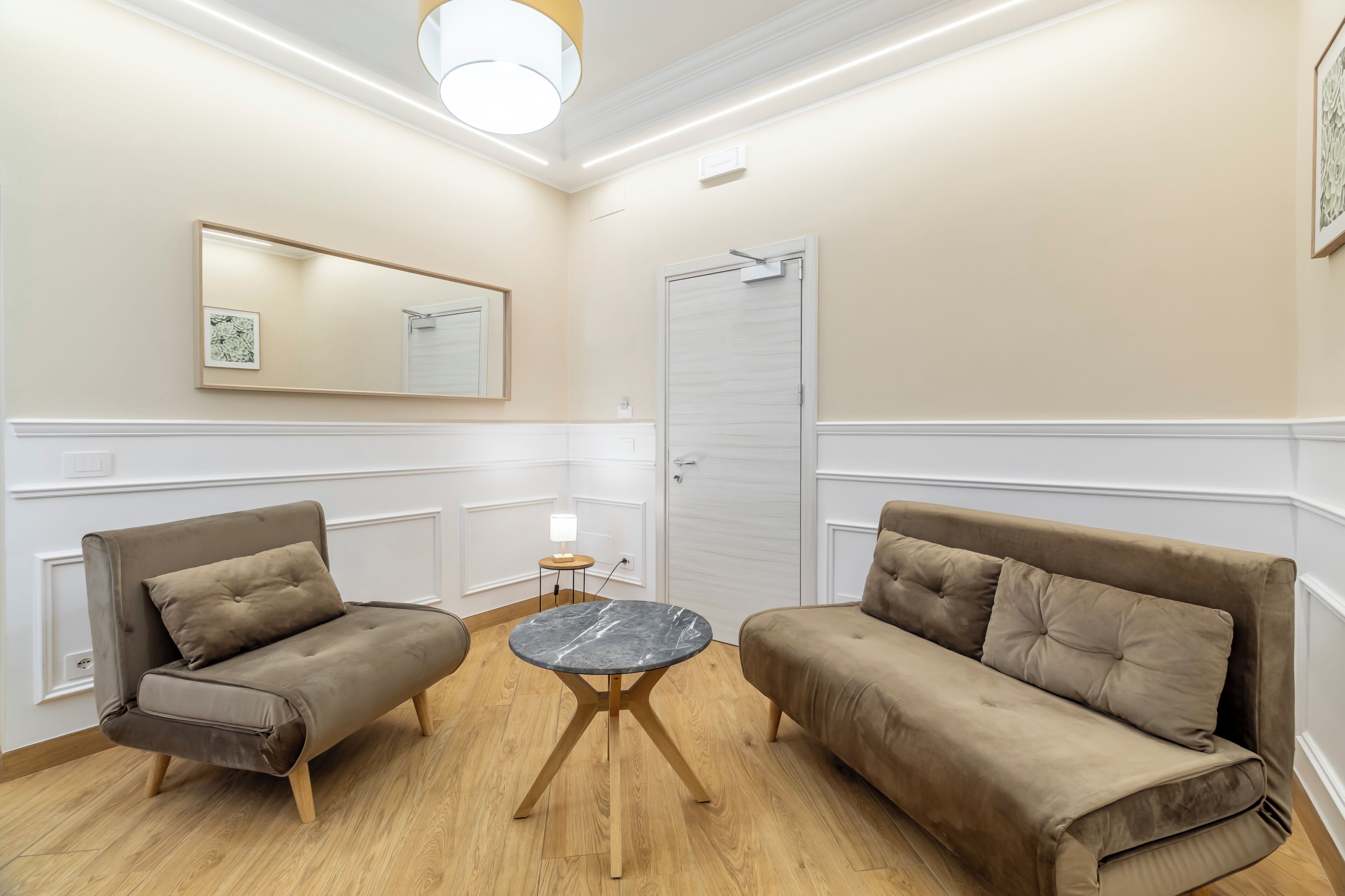A room with two sofas, a round table, a mirror, and a door.