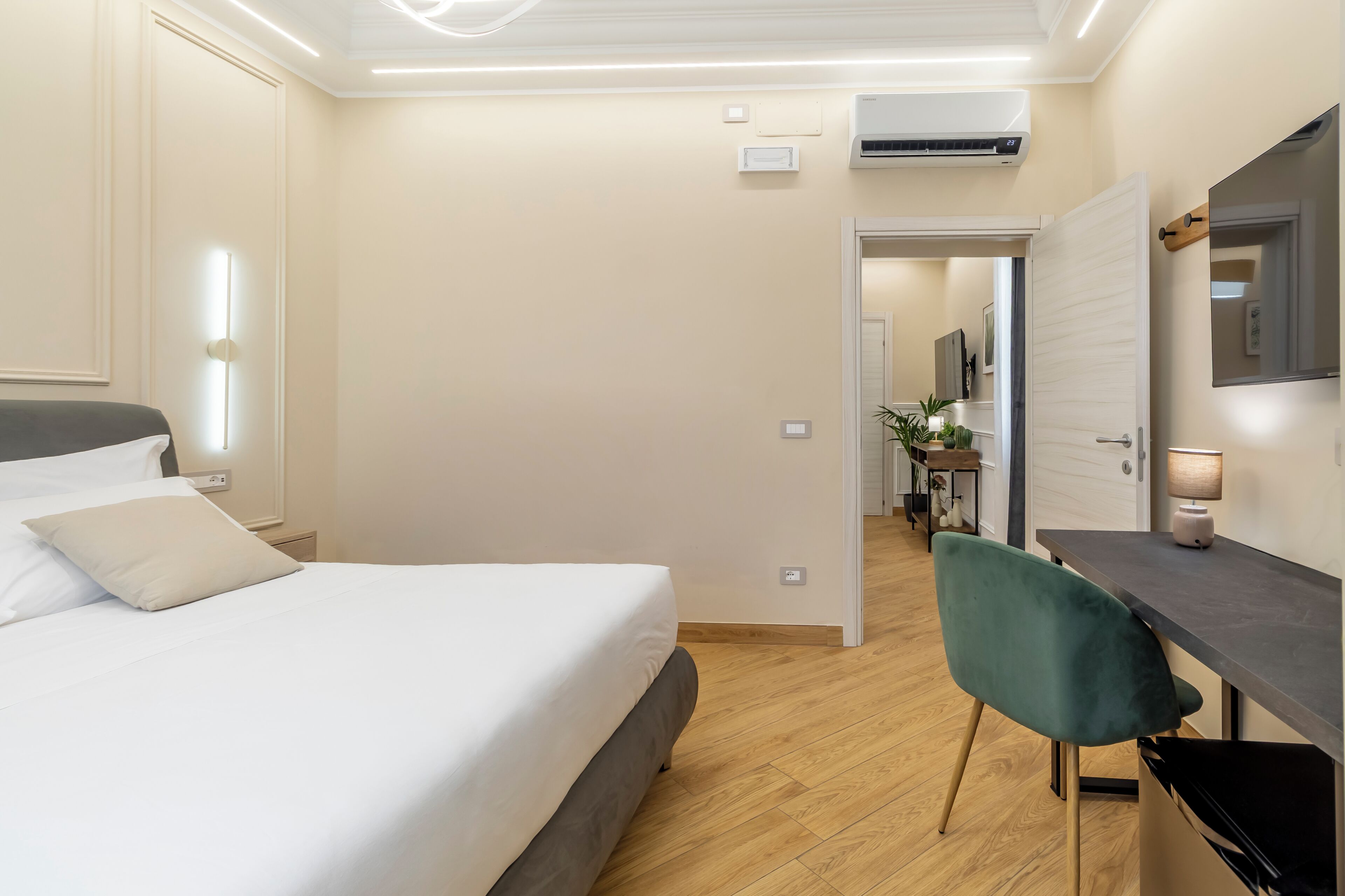 Une chambre d’hôtel comprenant un lit, une table de chevet, un bureau, une chaise et une porte ouverte donnant sur un couloir.
