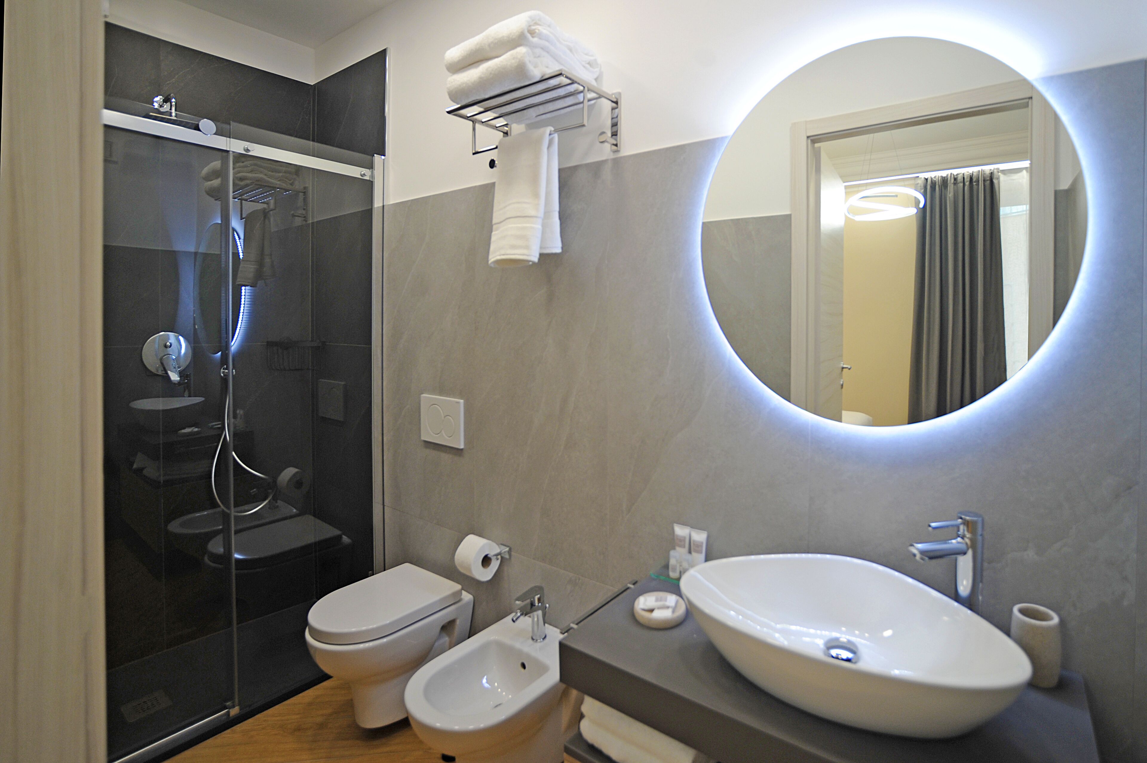 A modern bathroom with a glass-enclosed shower, a bidet, a toilet, and a large oval sink.