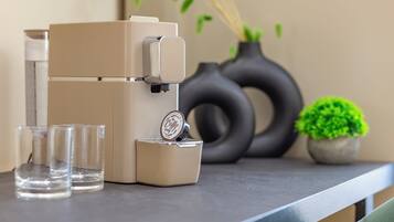 A coffee machine on a countertop with two glasses and a small potted plant.