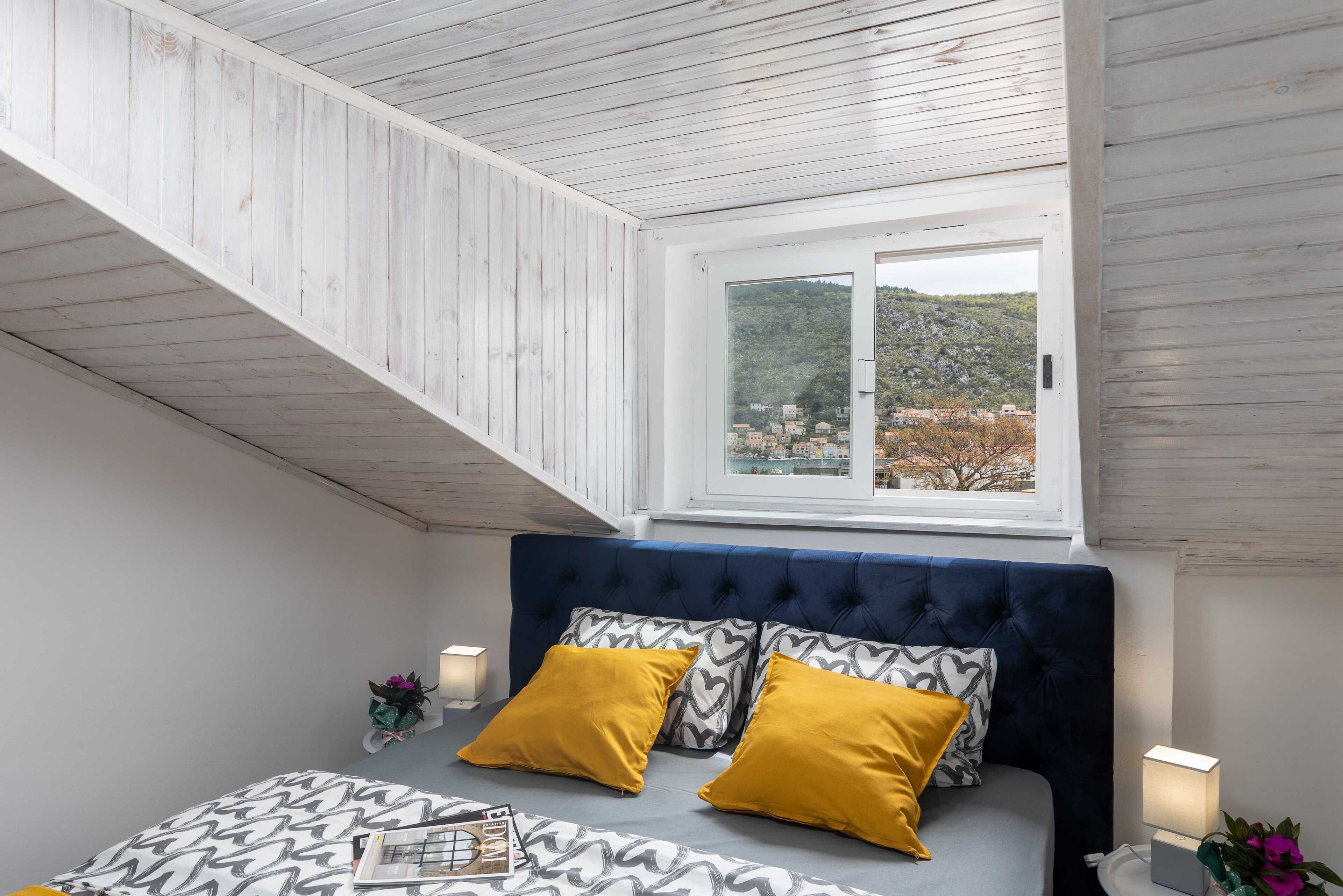 A bedroom with a bed, two yellow pillows, a window with a view of a hillside, and a wooden ceiling.