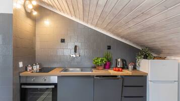 A kitchen with a wooden ceiling, grey tiles, a sink, a stove, and a refrigerator.