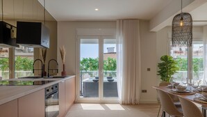 Una cocina moderna con una isla grande, puertas correderas de vidrio a un balcón y un comedor con alfombra redonda y sillas de mimbre.