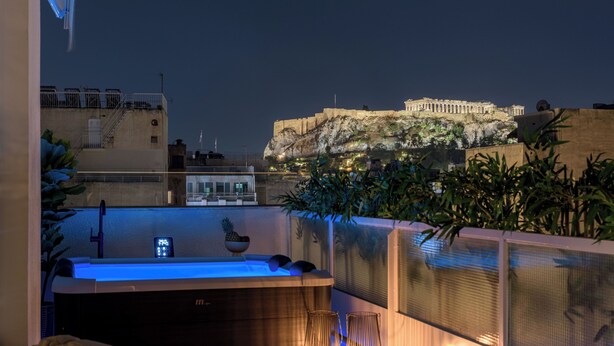 Una terraza en la azotea con jacuzzi, velas y vistas a un edificio histórico.