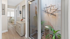A hallway with a sliding glass door leading to a bedroom, a small cabinet with a vase, and a decorative wall piece. - ☀️Updated Townhome, Close to Beach-Private Fenced Backyard-Sea Mist Getaway☀️ (New Smyrna Beach)