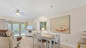 A dining area with a table and chairs, a ceiling fan, a television, and a large painting on the wall. - ☀️Updated Townhome, Close to Beach-Private Fenced Backyard-Sea Mist Getaway☀️ (New Smyrna Beach)