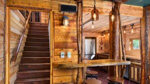 A wooden interior with a staircase, wooden bar counter, stools, and hanging light fixtures. - Cabin with Pikes Views, Fireplace, Walk to Wine (El Paso County)