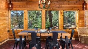 A wooden cabin interior with a dining table, chairs, and a chandelier. - Cabin with Pikes Views, Fireplace, Walk to Wine (El Paso County)