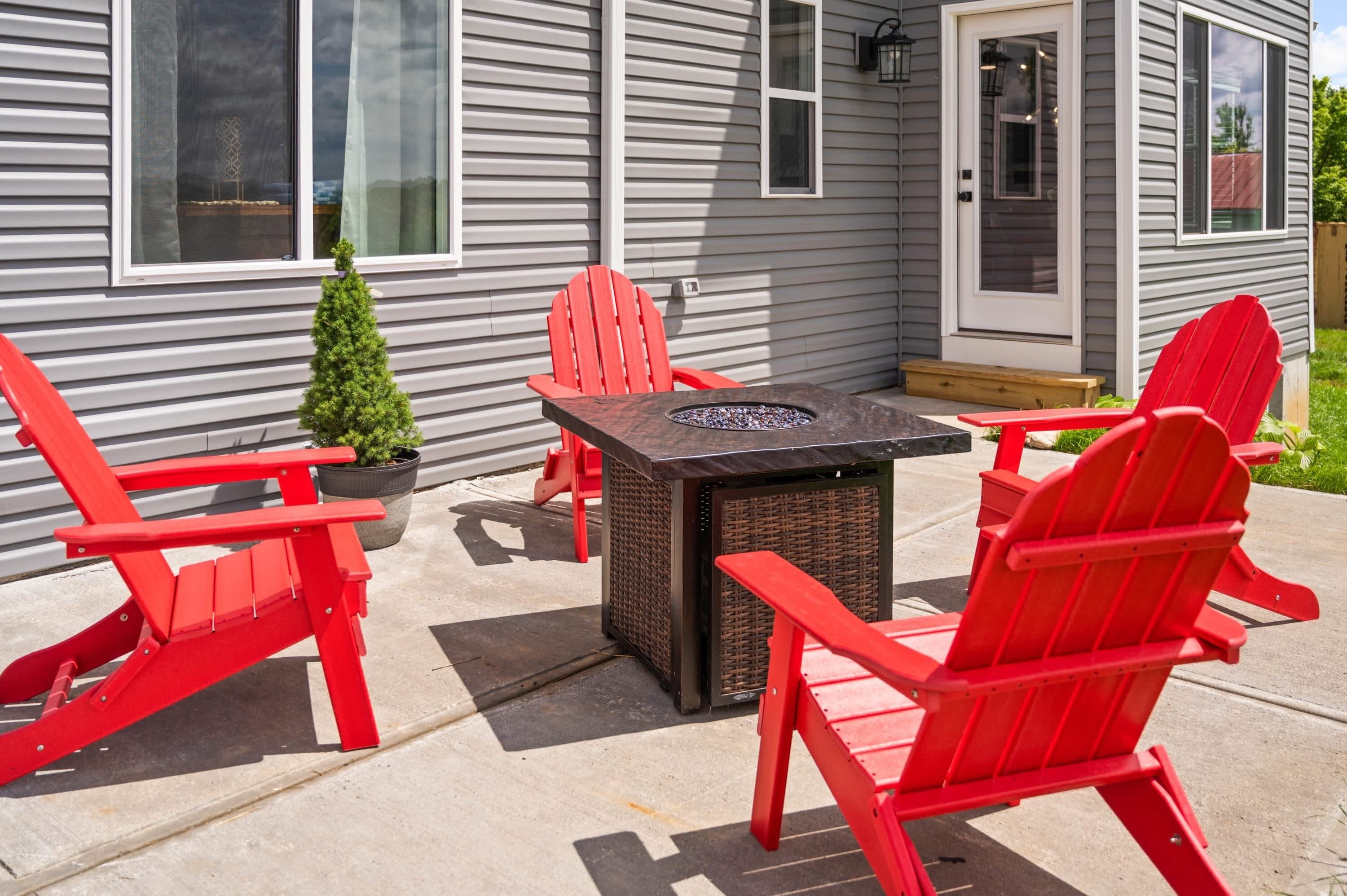 Une terrasse avec des fauteuils Adirondack rouges, une petite plante en pot et une table avec un foyer intégré.