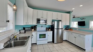Una cocina moderna con armarios blancos, electrodomésticos de acero inoxidable y una pared de acento color turquesa.