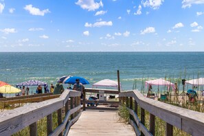 Une promenade en bois qui mène aux parasols et aux personnes qui se prélassent sur la plage.