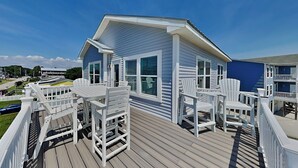 Un edificio azul con barandillas blancas y sillas de deck en una terraza de madera.