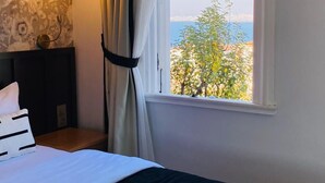 Ein Schlafzimmer mit einem Bett, einem Nachttisch, einer Lampe und einem Fenster mit Blick auf Grünflächen und ein Gewässer.
