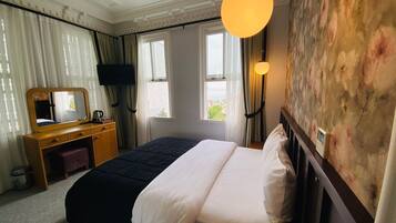 A hotel room with a bed, a wooden dresser, a mirror, a flat-screen TV, and a large window with curtains.