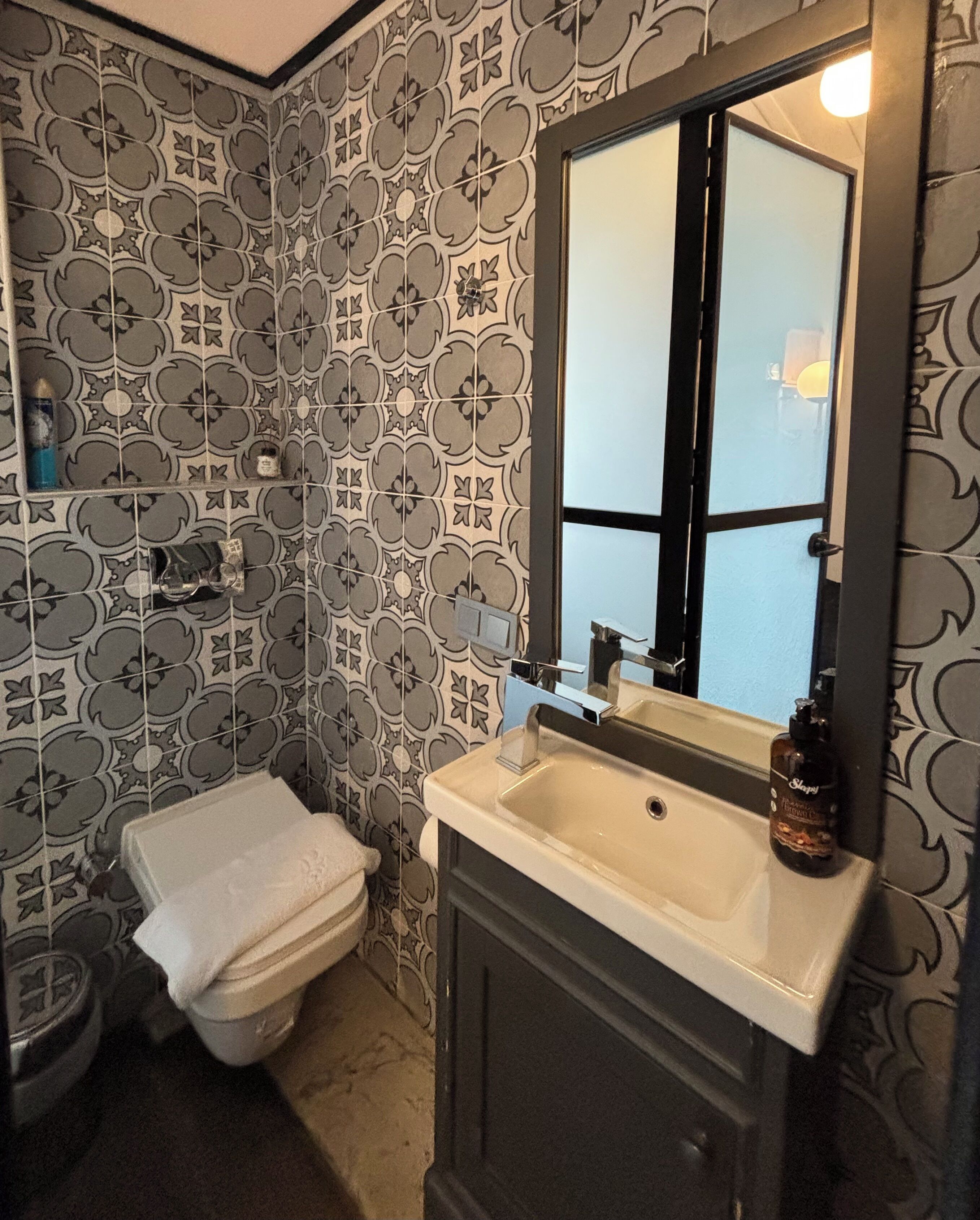 A bathroom with patterned tiles, a white sink, and a mirror.