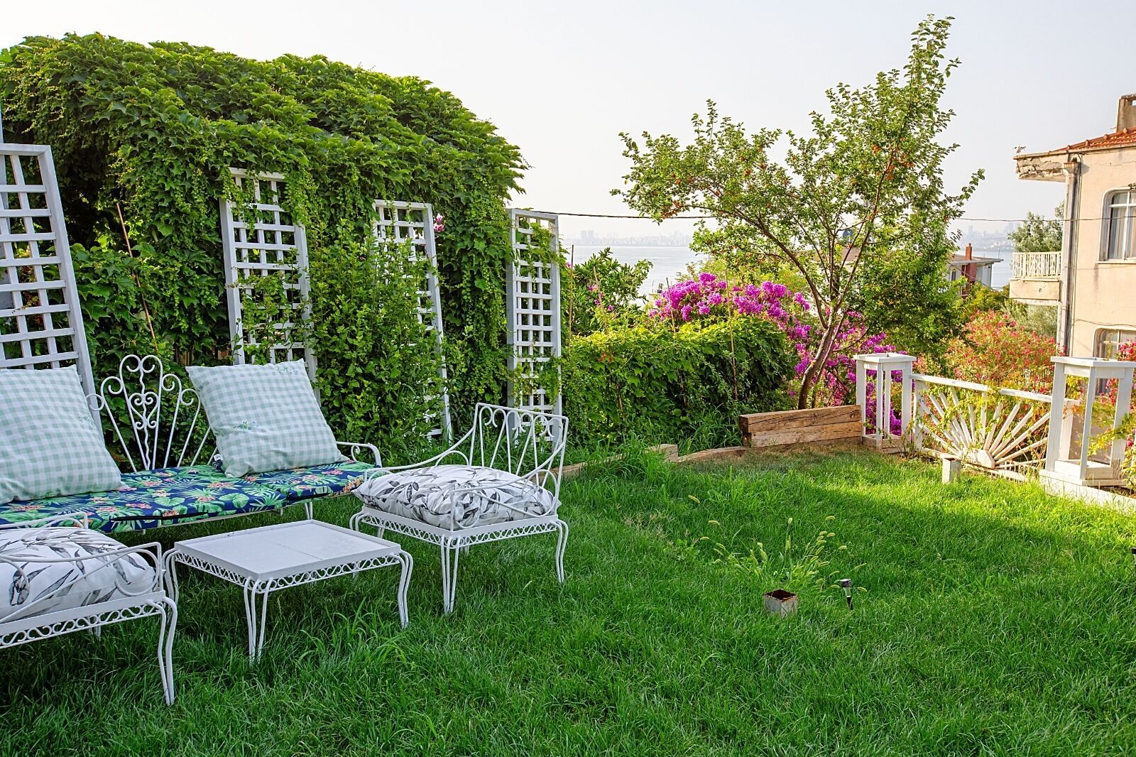 A garden with a white metal bench, a white metal table, and a white trellis structure.